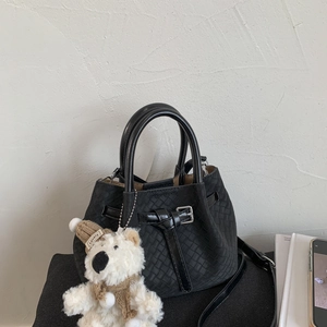 Detail of black woven leather bucket bag with cute plush bear charm and handle