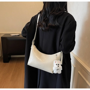 Detail of white crescent shoulder bag with pleated leather and plush dog charm accessory