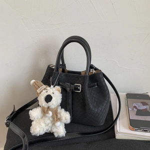 Detailed view of black woven texture tote bag with buckle and plush bear charm