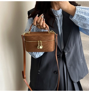 Brown quilted vanity case bag with top handle and gold chain zipper on model