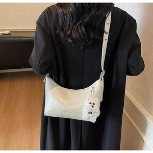 Detail view of off-white crescent underarm bag with cute plush puppy charm on black blazer
