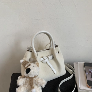 Detail view of white woven bucket bag with long strap and cute plush teddy bear charm
