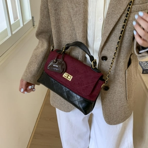 Close-up of wine red suede and black leather crossbody bag with chain and logo charm