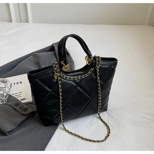Detailed macro view of black quilted tote bag with golden chain and metallic zipper
