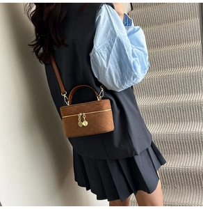 Close-up of brown quilted suede box bag featuring gold-tone zippers and a leather strap