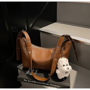 Detailed view of a brown pleated underarm bag with silver eyelets and a plush charm