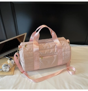 Close-up of pink quilted cylindrical travel bag with gold zippers and adjustable strap