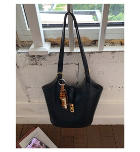 Detail of black faux leather tote with golden lock and vintage wooden bead tassel ornament
