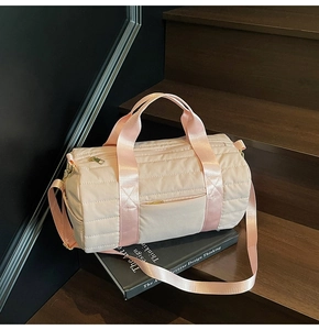 Pink quilted cylindrical travel bag with top handles and adjustable shoulder strap