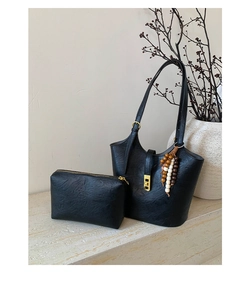 Detail of black textured bucket bag with gold lock and beaded charm on marble surface