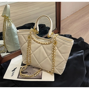 Detailed view of white quilted tote bag with gold chain strap on black silk fabric
