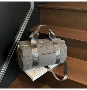 Detailed view of gray quilted travel duffel bag with gold hardware on wooden stairs