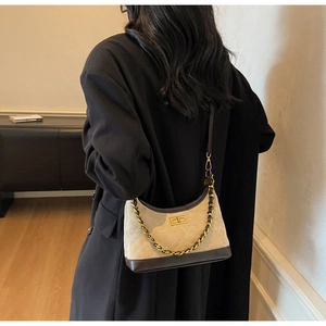 Detail of quilted suede underarm bag with gold chain strap on a black blazer