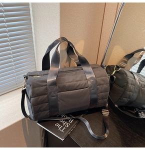 Detail of grey quilted cylinder travel bag with gold zippers and adjustable strap