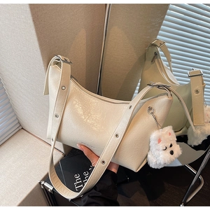 Close-up of off-white cracked leather shoulder bag with plush dog charm and silver zipper