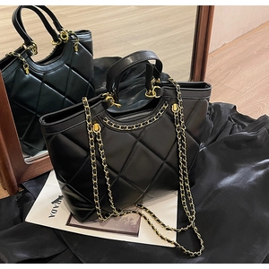 Detailed close-up of black quilted tote bag with chain strap on dark silk background