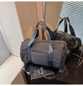 Detail of dark grey quilted cylinder travel bag with nylon straps and golden hardware