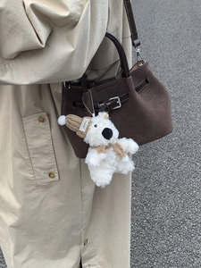 White teddy bear charm with brown knit hat and scarf hanging on a brown handbag