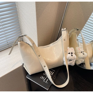 Detail of cream crescent shoulder bag with pleated leather texture and a plush charm