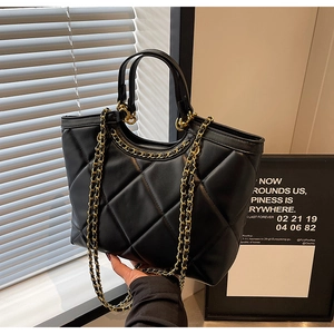 Close-up of black quilted texture and golden chain details on large tote bag