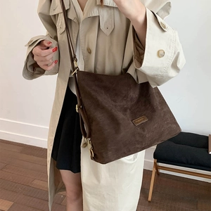 Detail of dark brown matte tote bag with adjustable strap and metal logo on autumn trench coat