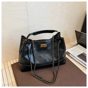 Detail of black quilted tote bag with gold chain strap and metal twist lock on a desk