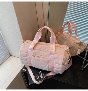 Detailed close-up of pink quilted cylindrical gym bag with golden metal zipper and straps
