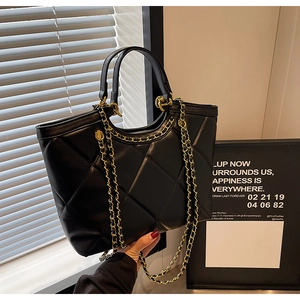 Detailed close-up of black quilted leather tote bag with gold chain strap detail