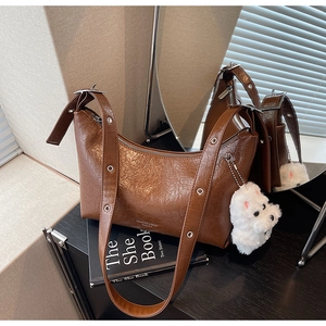 Detail of a brown pleated leather bag with a plush cat charm on a stack of books
