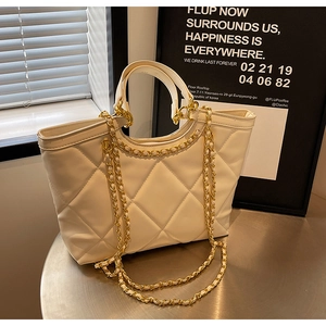 Detail of quilted beige tote bag with light gold chain strap on metallic surface