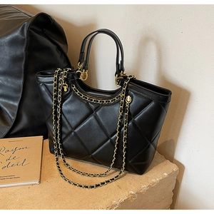 Detail of black quilted leather tote bag with gold chain strap on a stone pedestal