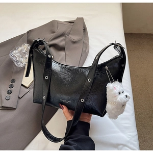 Detail of black crinkled leather underarm bag with silver grommets and plush dog charm