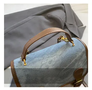 Detail of blue denim and brown leather handbag handle with gold metal ring buckles