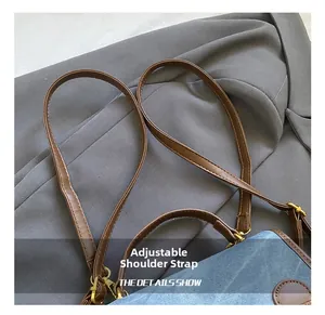 Detail of adjustable brown leather shoulder strap with golden metal buckle on denim backpack