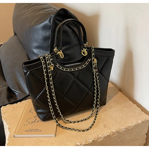 Detailed macro view of quilted faux leather texture and gold chain strap on black tote bag