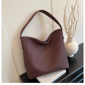 Detail shot of large dark brown tote bag with wide strap on a minimalist wooden surface