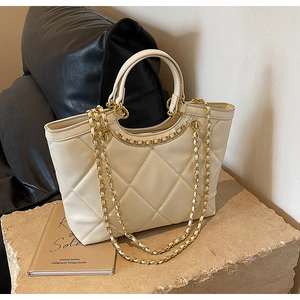 Detail of off-white quilted tote bag with gold chain strap on a stone pedestal