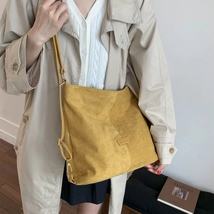 Detail of a ginger yellow suede bucket bag with adjustable strap worn by a model
