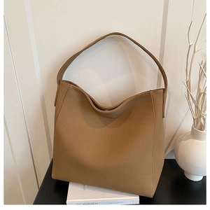 Detailed view of dark camel tote bag with wide strap on a minimalist desk setting