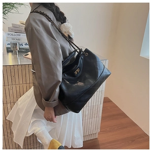 Detail of black quilted tote bag featuring gold chain strap and metal turn-lock closure