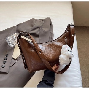 Close-up of dark brown crescent bag with oily leather texture and white plush bear charm