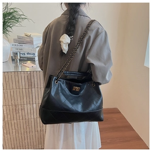Detailed view of black quilted tote bag with chain strap and gold twist lock on shoulder