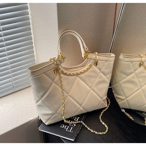 Detail of cream quilted tote bag featuring classic diamond stitching and gold chain strap