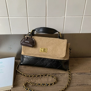 Detail of two-tone crossbody bag with gold twist lock and mini brand charm on wood surface