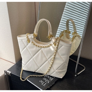 Detail of white quilted tote bag featuring gold chain strap and elegant faux leather texture