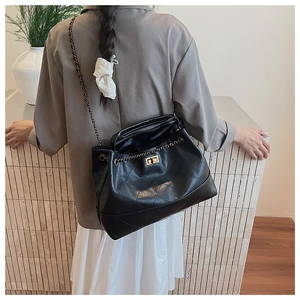 Detail of black quilted tote bag with metallic chain strap and rectangular turn-lock closure
