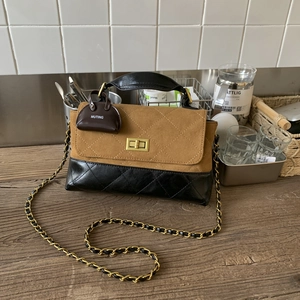 Detail view of the elegant mixed-material shoulder bag with a gold turn-lock and chain strap