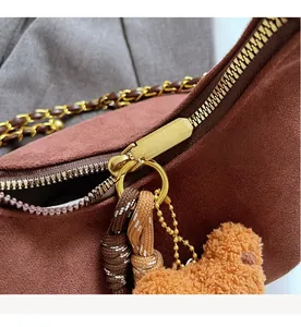 Detail view of the smooth gold zipper and bear charm on the brown suede shoulder bag