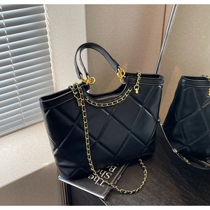Detail of black quilted tote bag with gold chain strap and spacious interior design