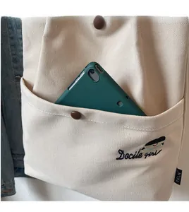 Close-up of cream canvas tote bag showing front pocket holding a green tablet device